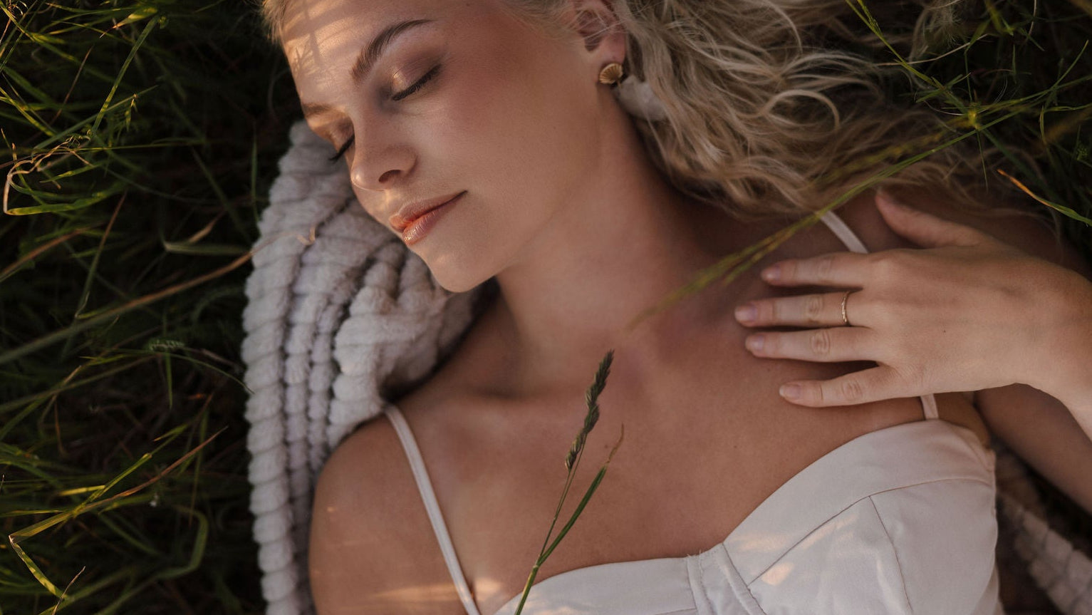 Woman lying on grass with a blanket, wearing a white dress.